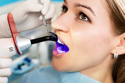 A woman receiving dental treatment, with a dentist using a device to clean or inspect her teeth.