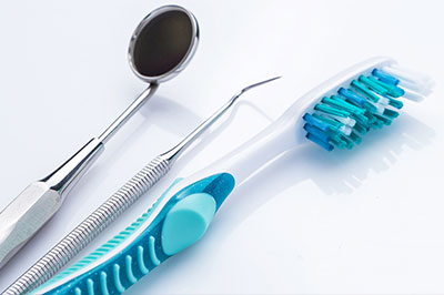 The image displays a collection of dental instruments, including a toothbrush and scissors, arranged on a white background.