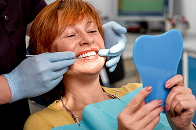 Woman in a dental chair with blue teeth guard, smiling and holding up a tooth impression.