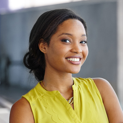 A smiling woman in a yellow top, posing for a portrait with a building in the background.