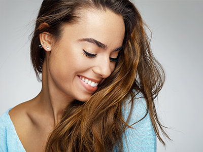 The image shows a woman with long hair, wearing a light-colored top, smiling and looking off to the side.