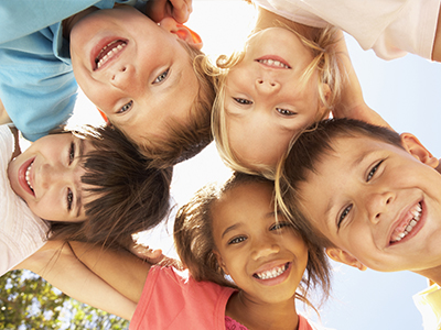 The image is a photograph of a group of children, likely taken during the daytime outdoors, smiling and posing for the camera.