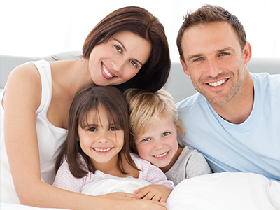 A family of five, including a man, woman, and three children, is smiling together in bed.