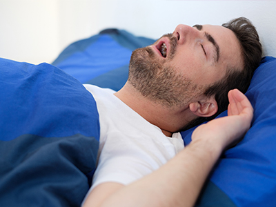 A man is lying in bed, appearing to be asleep or resting with his mouth open.